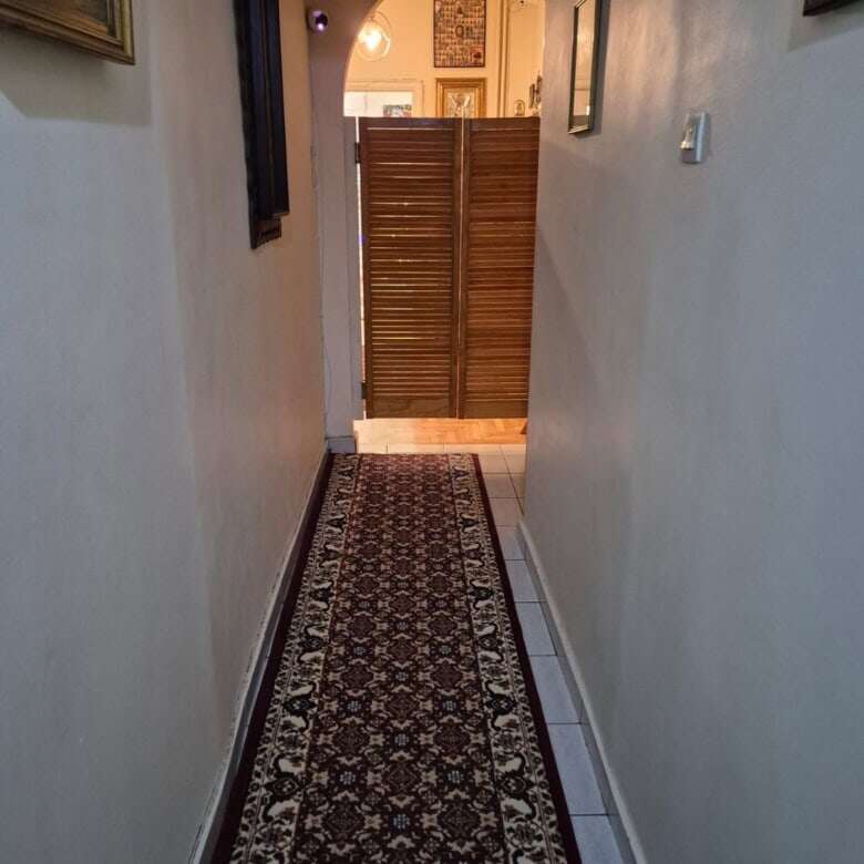 Interior view of a narrow hallway in an Athens apartment with a patterned rug and framed art pieces.