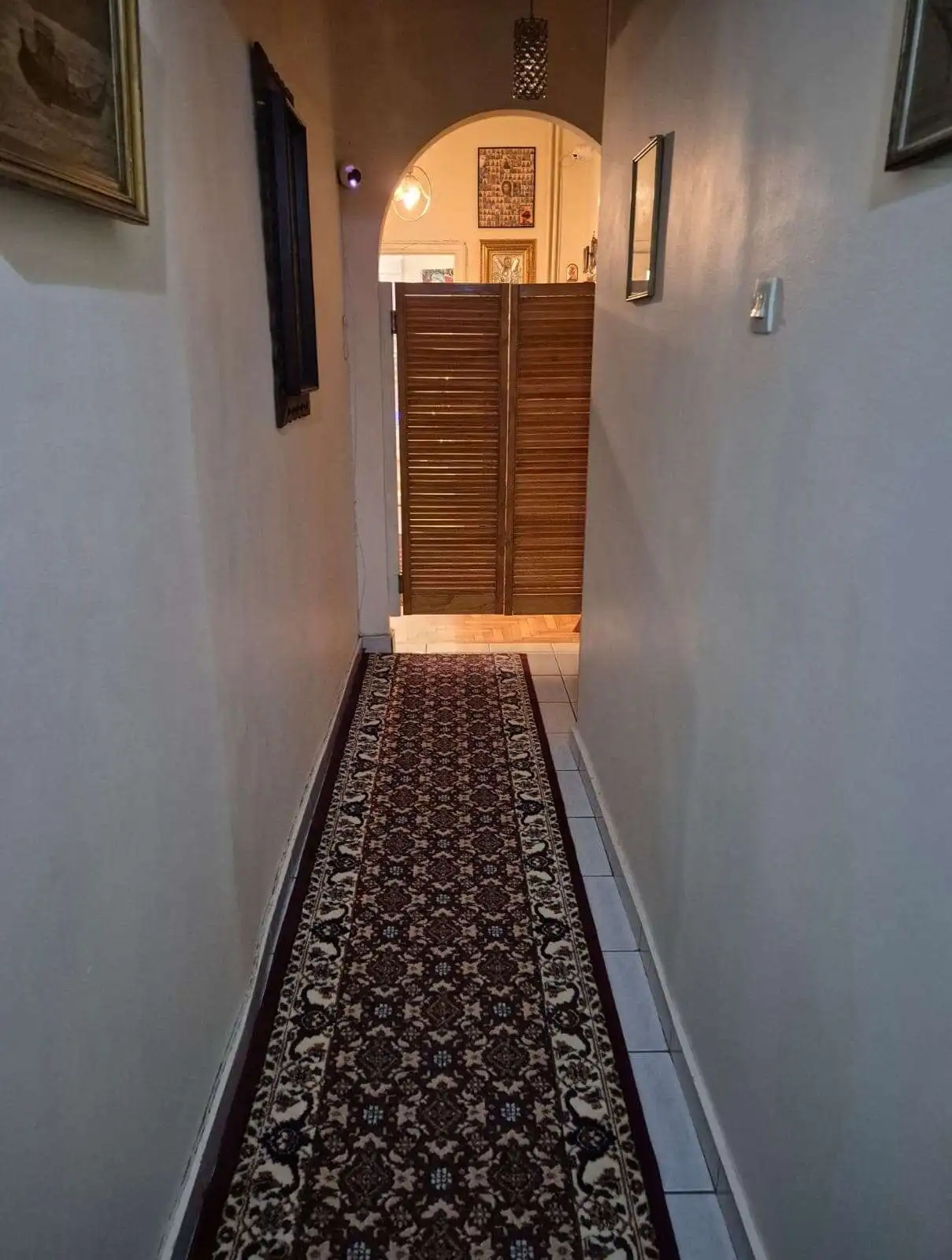 Interior view of a narrow hallway in an Athens apartment with a patterned rug and framed art pieces.