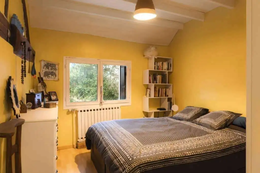 Bright bedroom with yellow walls and large window in a 6-bed estate in La Celle-sur-Morin.