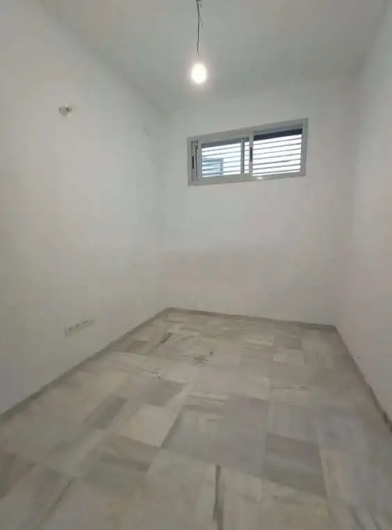 Small bedroom with white walls, marble floor, and a window for natural light.