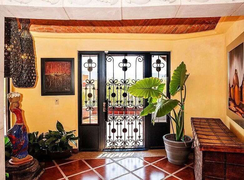Beautiful tropical villa entrance featuring ornate wrought iron gate and lush potted plants.