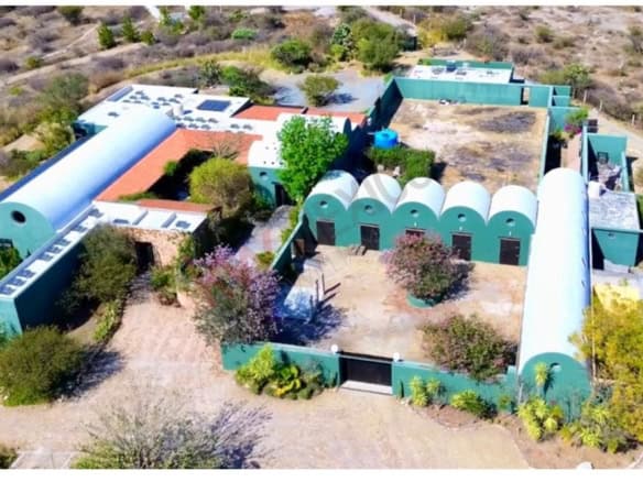 Aerial view of a distinctive desert property featuring several interconnected buildings and lush gre.