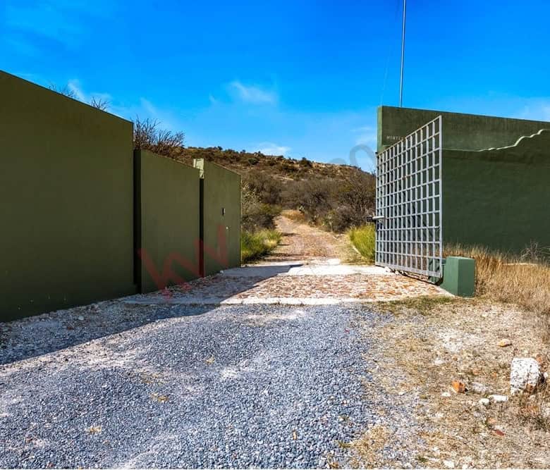 Gated entrance with green walls and metal gate in a rural landscape.