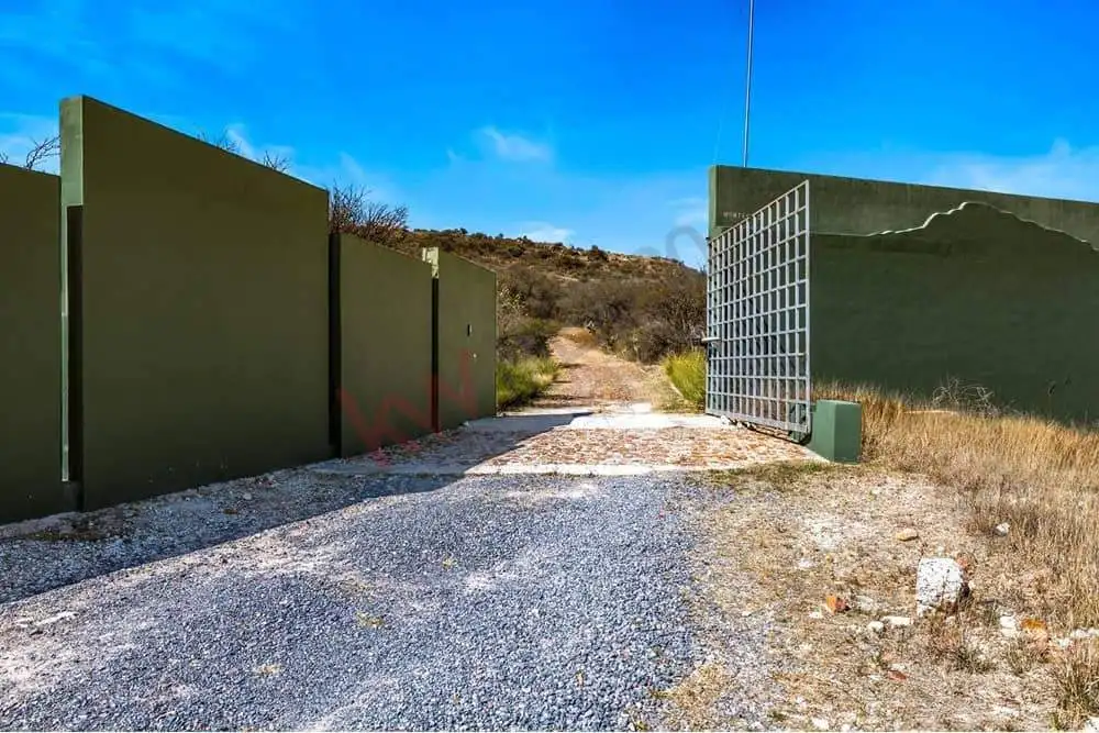 Gated entrance with green walls and metal gate in a rural landscape.
