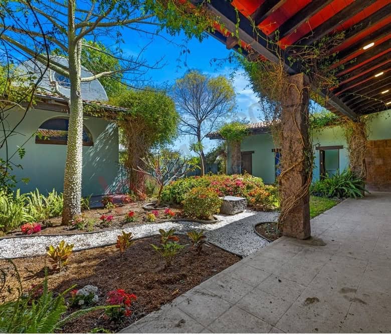 Beautiful garden courtyard featuring mature trees, colorful flowers, and a shaded patio area. Perfec.