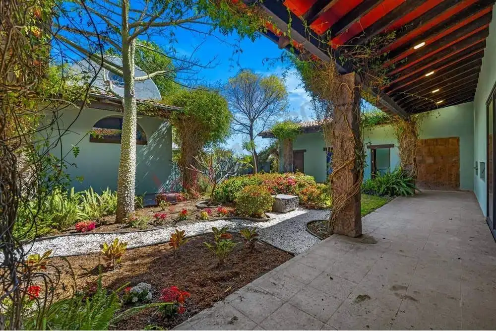 Beautiful garden courtyard featuring mature trees, colorful flowers, and a shaded patio area. Perfec.