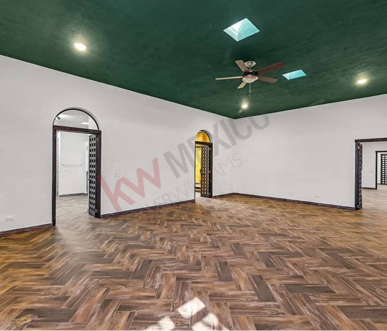 Spacious living room with wooden flooring, green ceiling, and multiple doorways for versatile use.