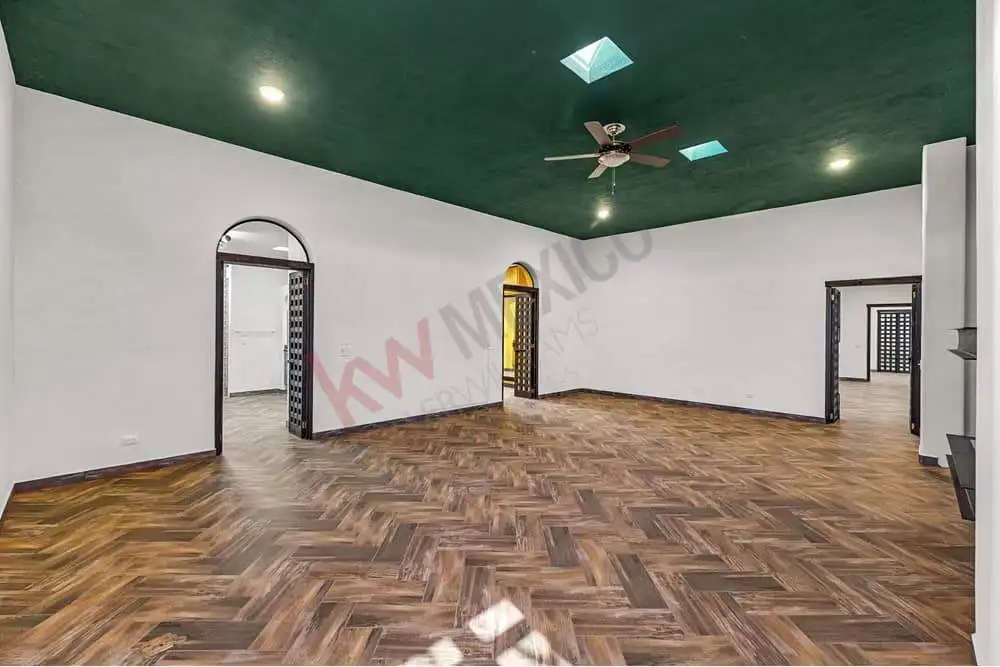 Spacious living room with wooden flooring, green ceiling, and multiple doorways for versatile use.