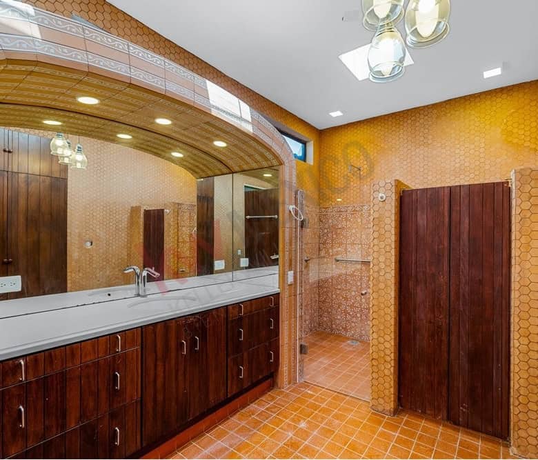 Spacious bathroom featuring wooden cabinets, a large mirror, and orange tile walls and floors.