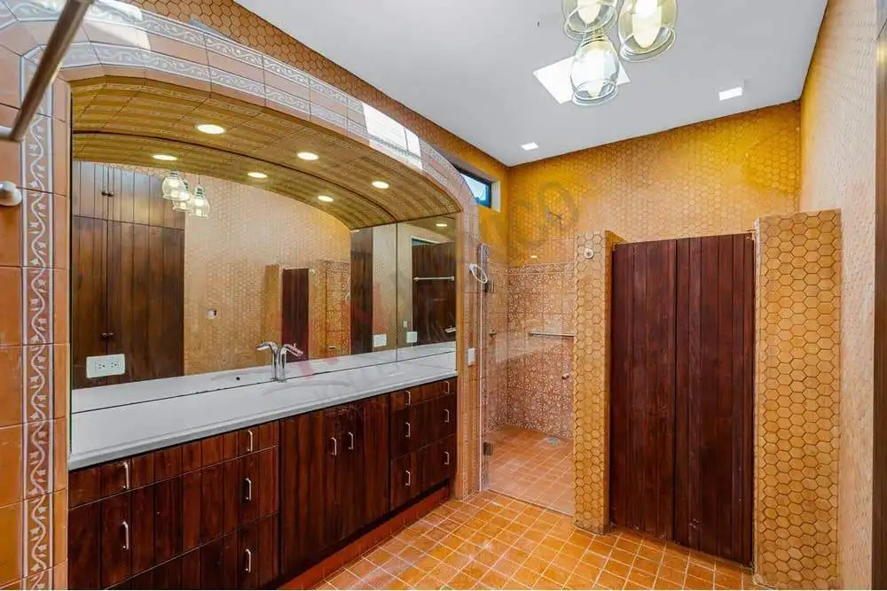 Spacious bathroom featuring wooden cabinets, a large mirror, and orange tile walls and floors.