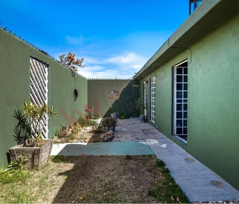 Modern green house exterior with garden and pathway under blue sky.