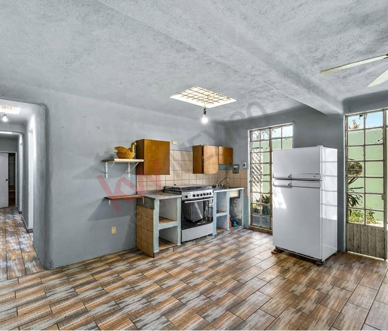 Bright kitchen with wooden cabinets, white refrigerator, and natural light from large windows.