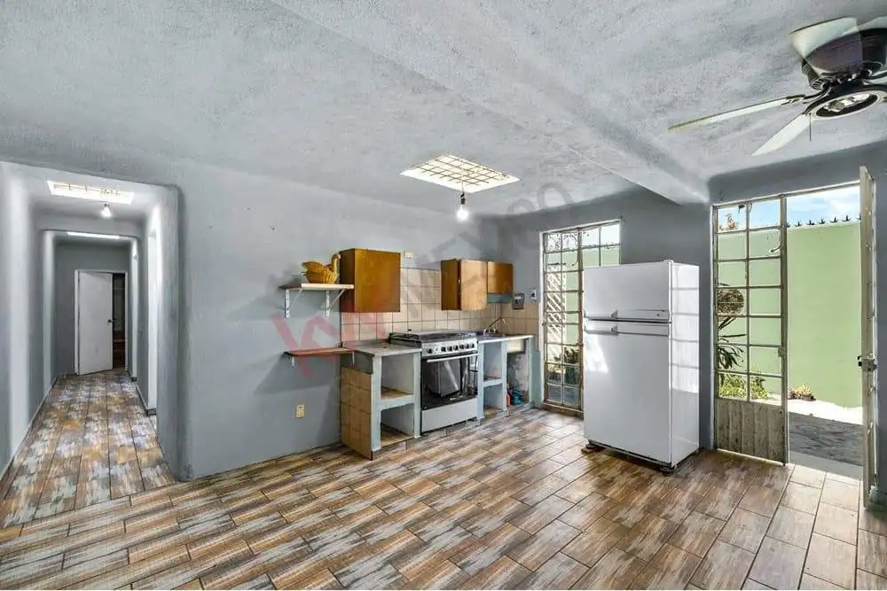 Bright kitchen with wooden cabinets, white refrigerator, and natural light from large windows.