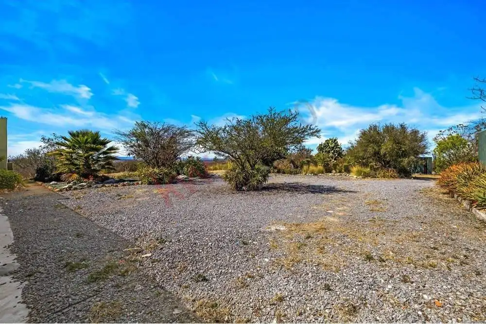 Desert plot with dry soil, scattered bushes, and trees under a bright blue sky, ideal for building o.
