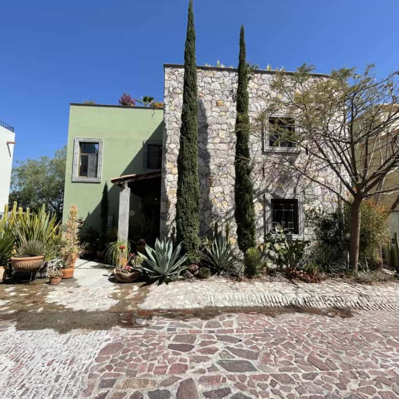 Beautiful Mediterranean-style house with stone and stucco facade, surrounded by lush plants and tall.