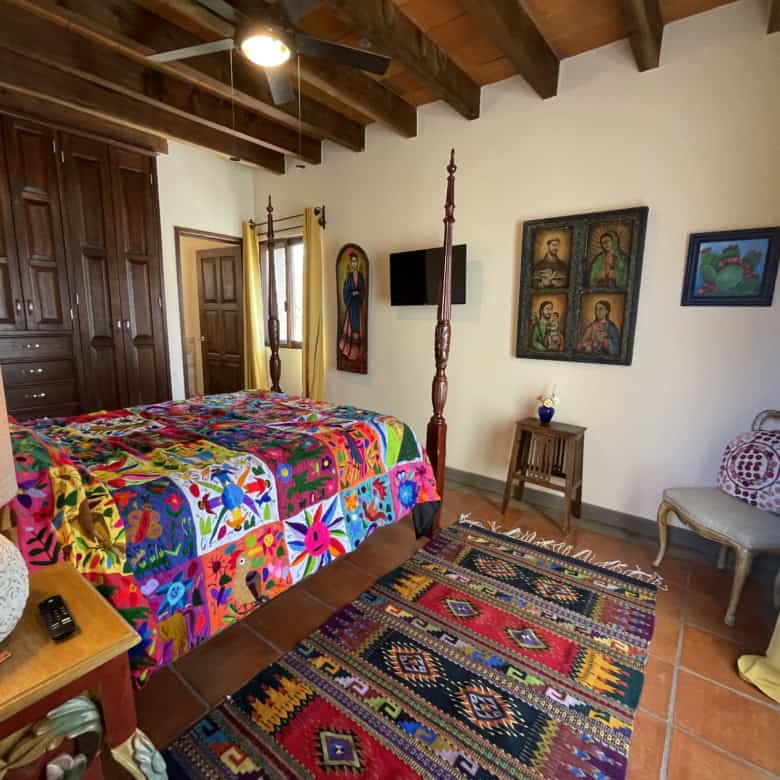 Charming bedroom featuring a vibrant quilt, wooden ceiling beams, and traditional furniture. Bright.