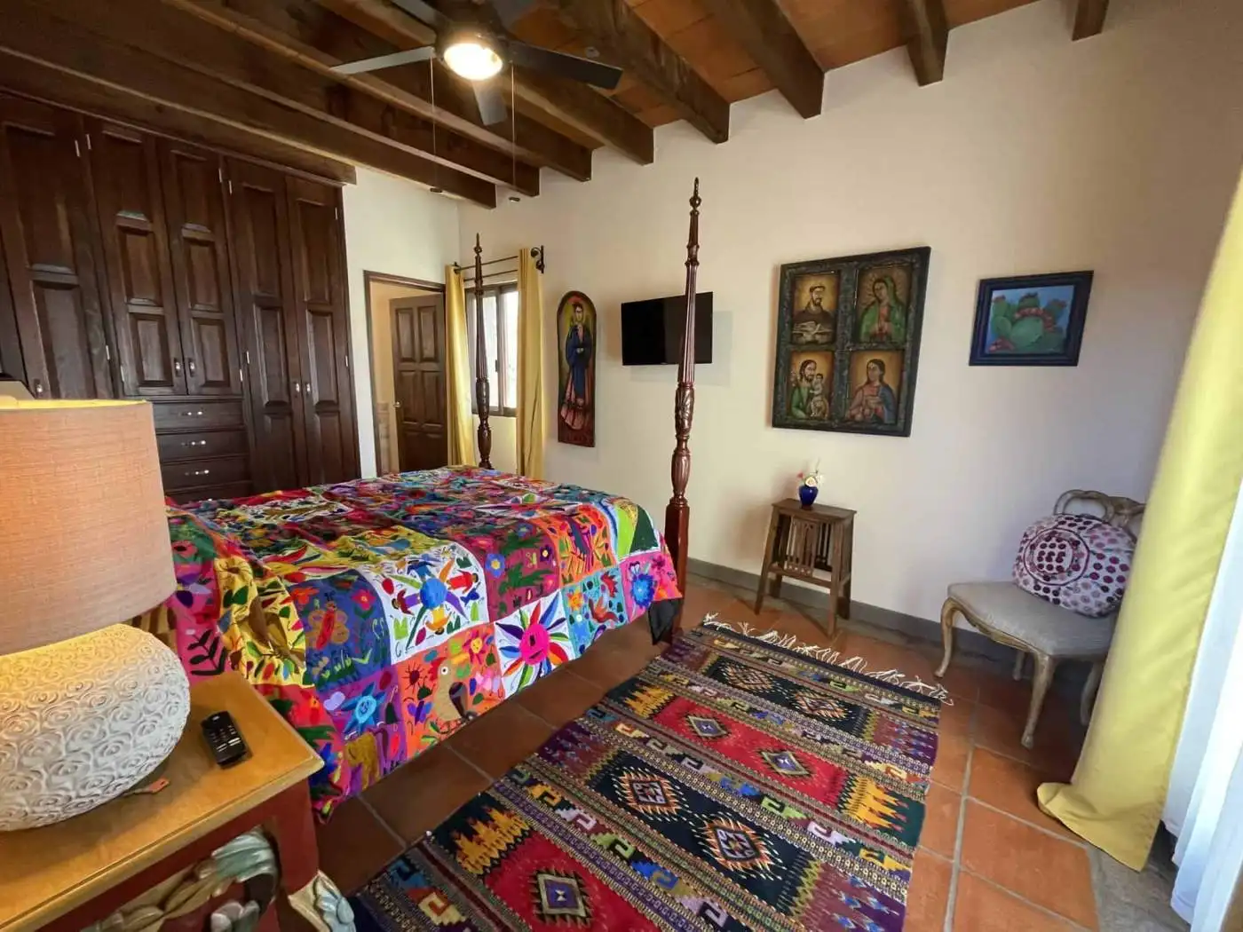 Charming bedroom featuring a vibrant quilt, wooden ceiling beams, and traditional furniture. Bright.