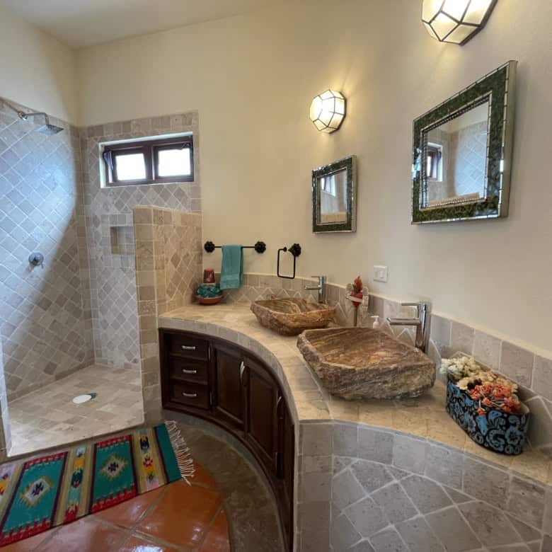 Luxury bathroom with stone sinks and walk-in shower, featuring modern fixtures and elegant decor.