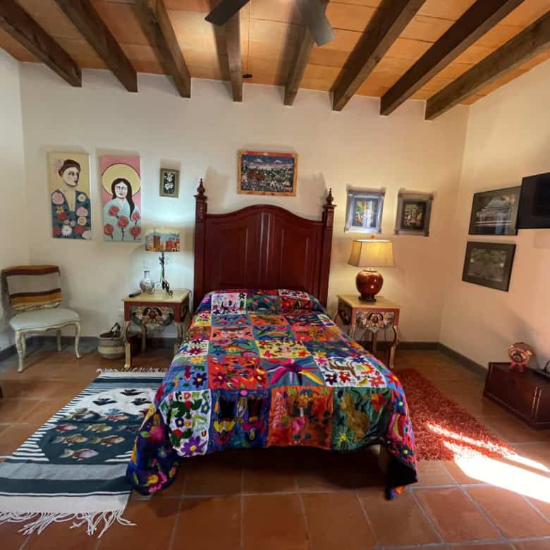 Cozy bedroom with vibrant quilt, wooden ceiling, and decorative art pieces.