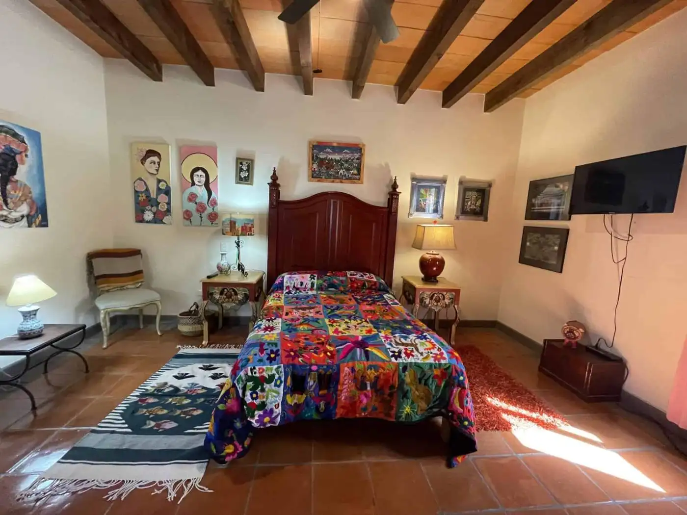 Cozy bedroom with vibrant quilt, wooden ceiling, and decorative art pieces.