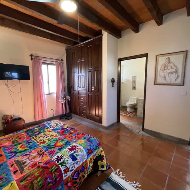 Comfortable bedroom with colorful quilt and wooden ceiling beams.