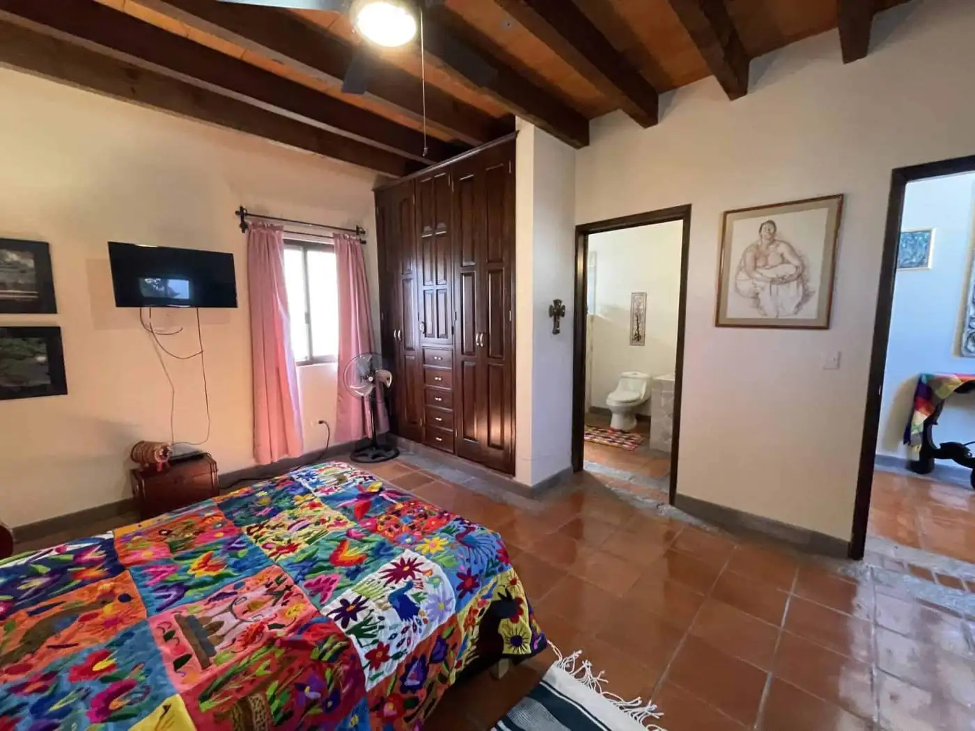 Comfortable bedroom with colorful quilt and wooden ceiling beams.