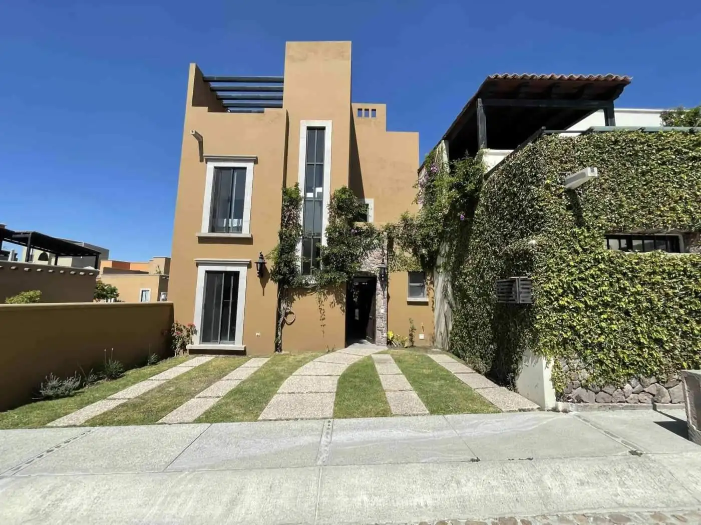 Modern beige residential building with landscaped front yard and clear blue sky.