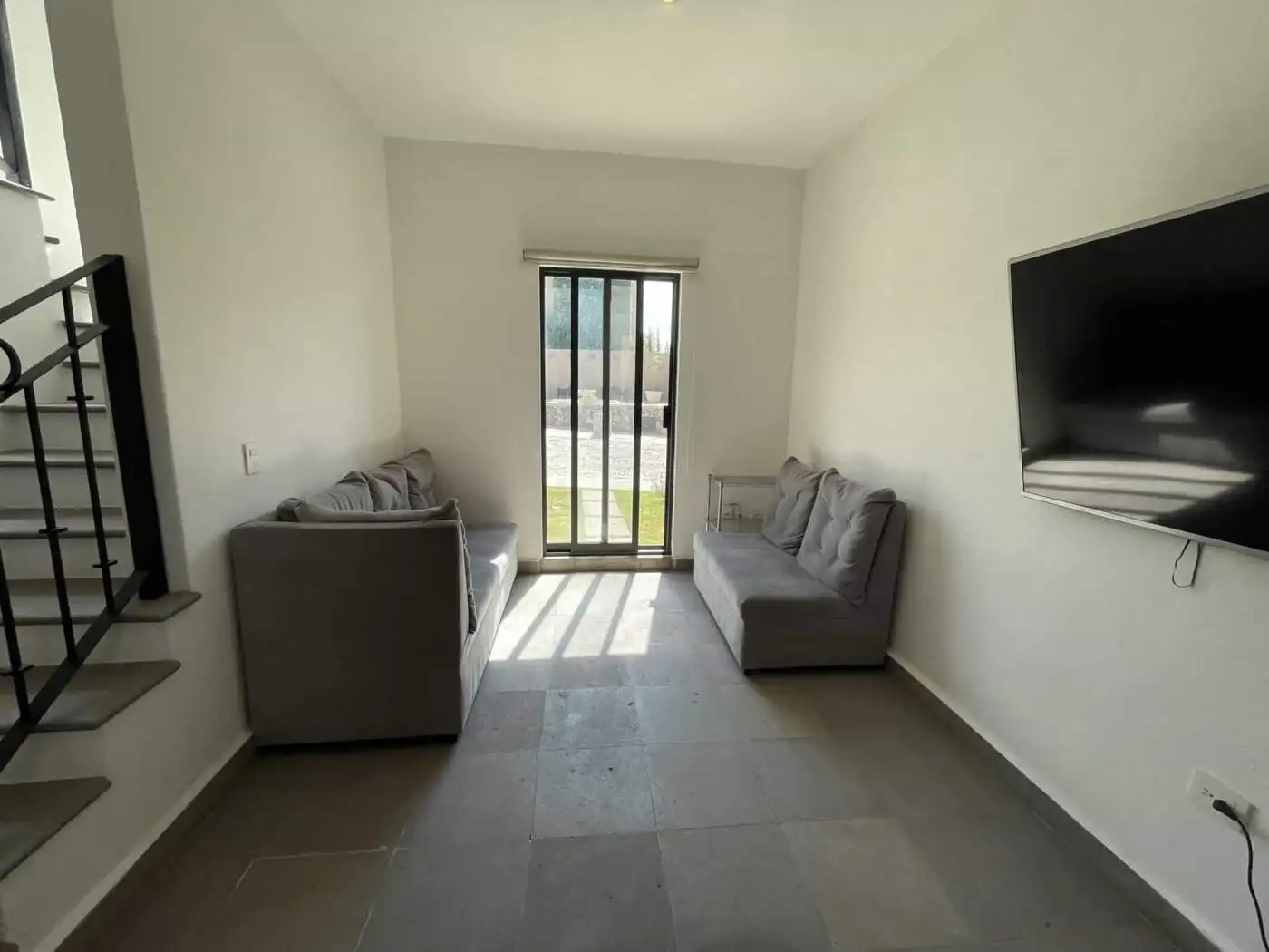 Modern living room with two gray sofas, sliding glass door, and wall-mounted TV.