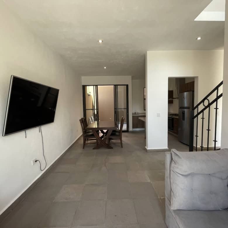 Bright living room with wall-mounted TV, dining table, and staircase in a contemporary home.