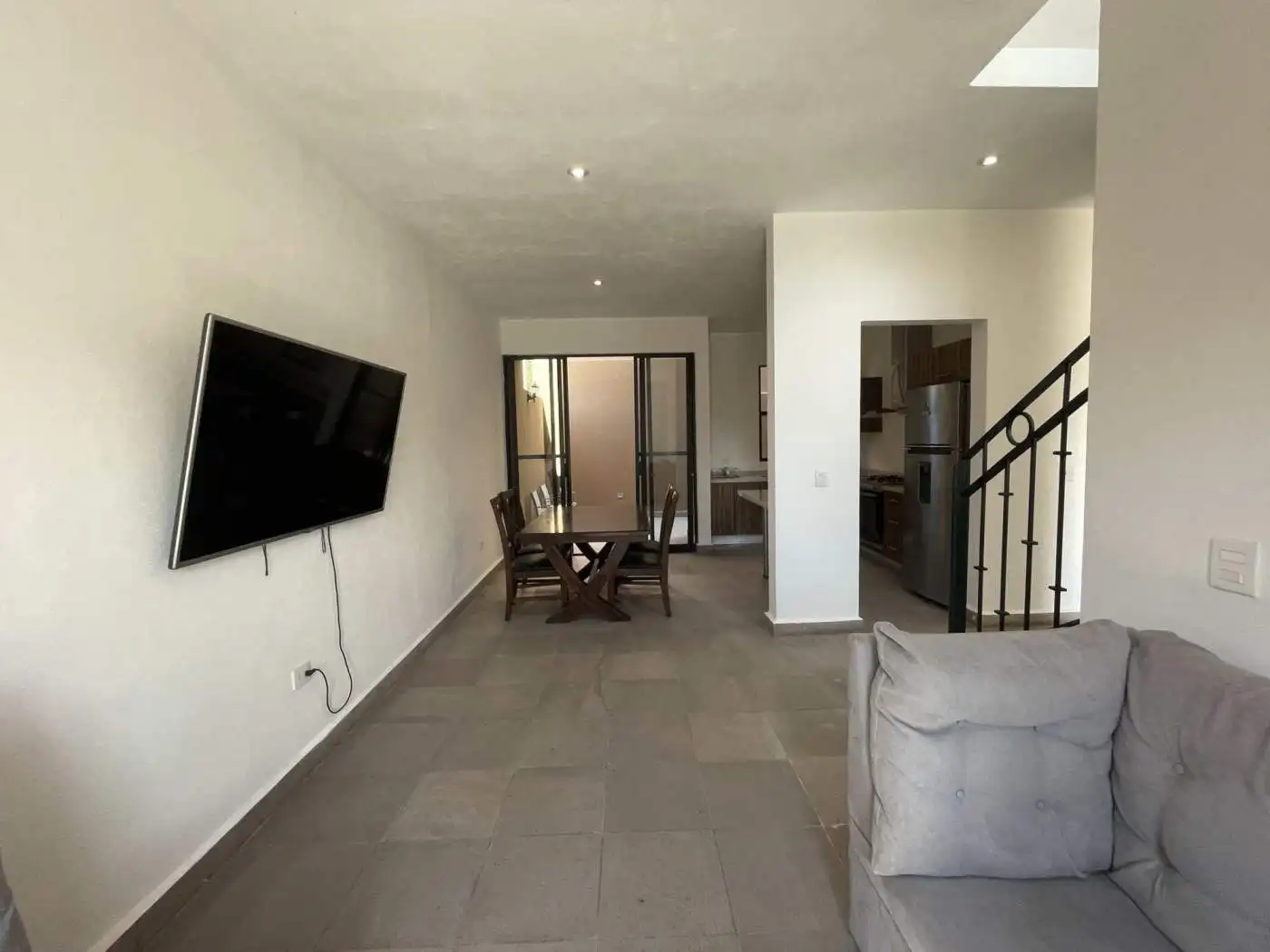 Bright living room with wall-mounted TV, dining table, and staircase in a contemporary home.