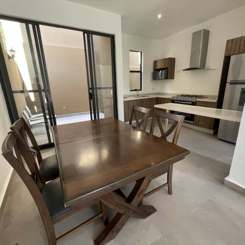Modern kitchen and dining room with wooden table, chairs, and contemporary appliances.
