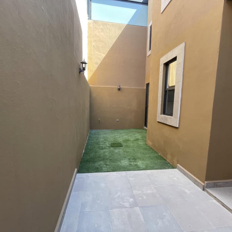 Backyard of a modern townhouse featuring artificial grass, beige exterior walls, and a small outdoor.
