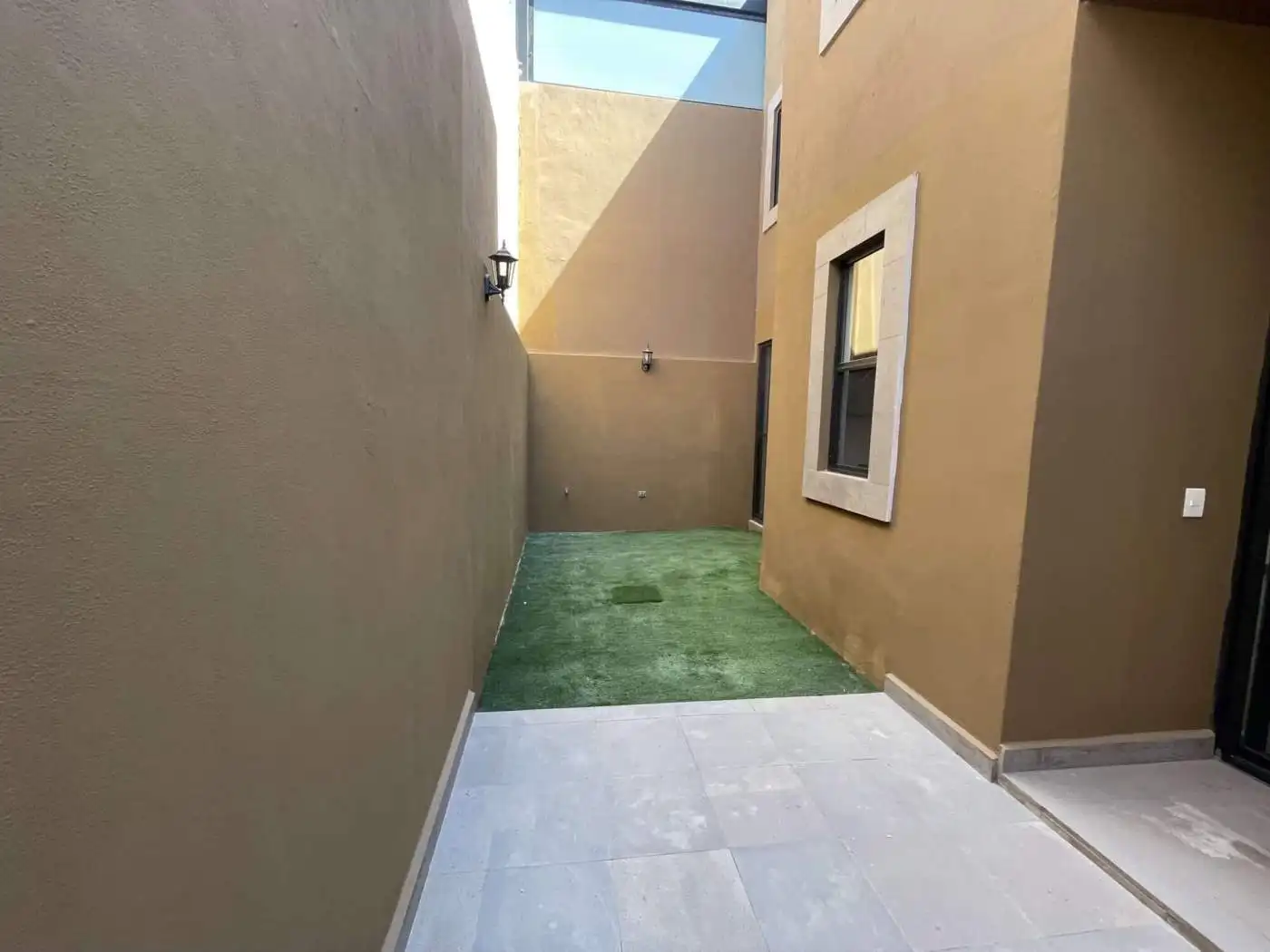 Backyard of a modern townhouse featuring artificial grass, beige exterior walls, and a small outdoor.