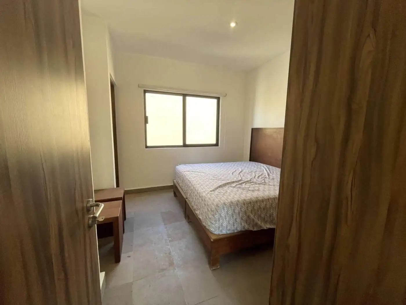 Bedroom with wooden bed frame, window, and minimal decor.