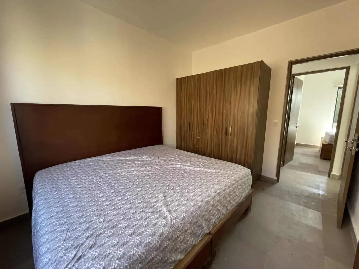 Spacious bedroom featuring a wooden bed frame and wardrobe, with an open door leading to another roo.