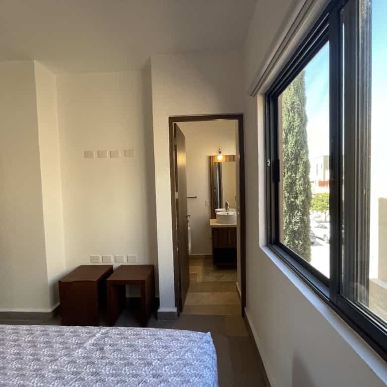 Modern bedroom with large window and en-suite bathroom for sale.