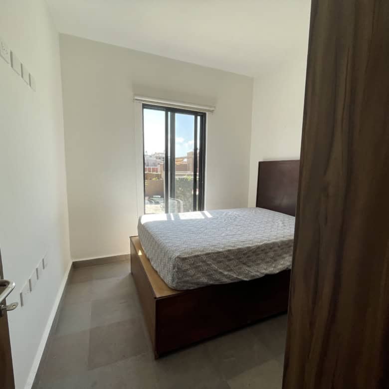 Modern bedroom with large window and wooden furniture, ideal for comfortable living in an internatio.