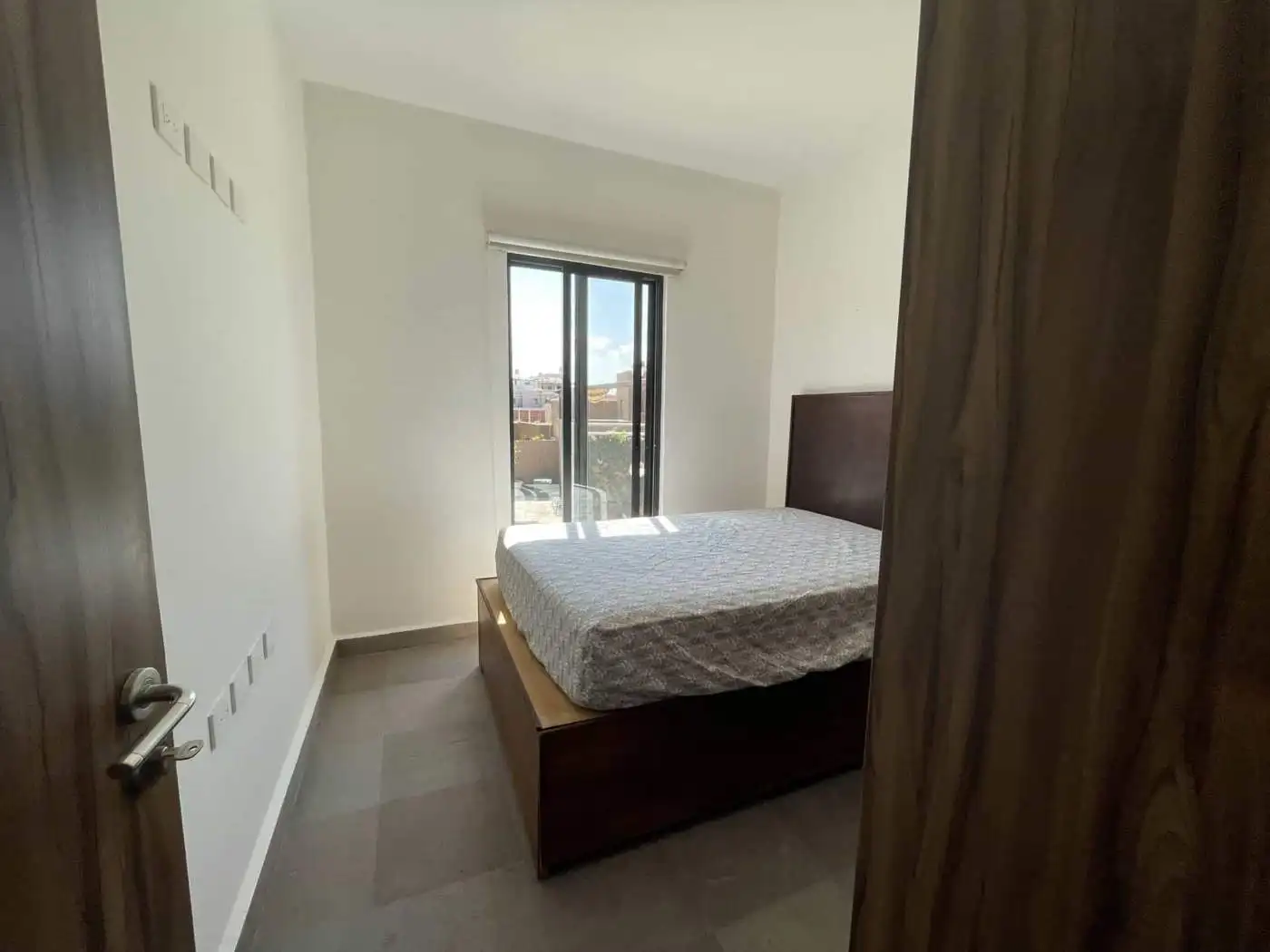 Modern bedroom with large window and wooden furniture, ideal for comfortable living in an internatio.