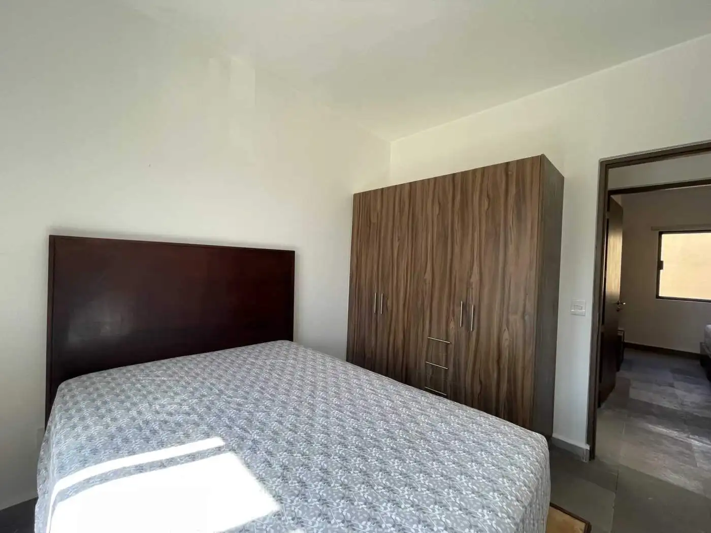 Spacious bedroom featuring a wooden wardrobe and sunlight streaming through the window.