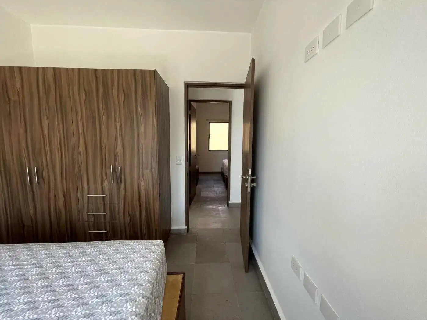 Bedroom with wooden wardrobe and open door leading to a bright interior space.