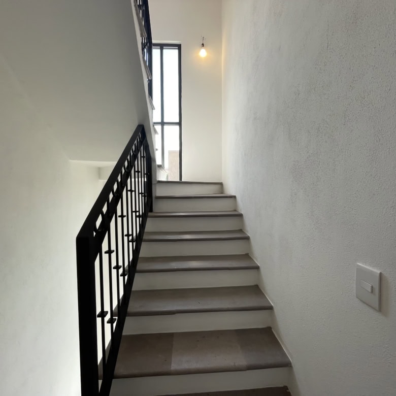 Interior staircase with black metal railing and bright natural light from window.