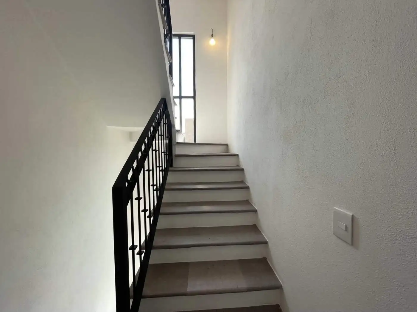 Interior staircase with black metal railing and bright natural light from window.