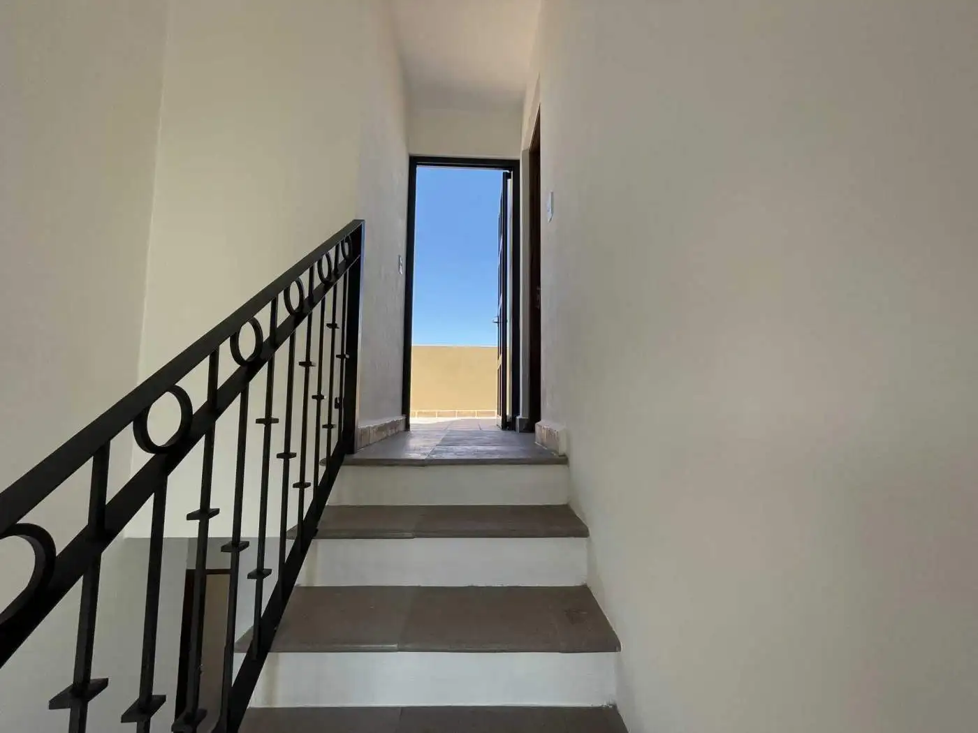 Interior staircase leading to an outdoor balcony or terrace with a view of the sky.