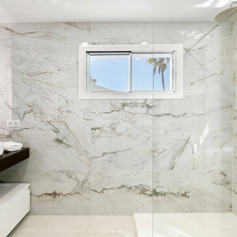 Modern marble bathroom with walk-in shower and ocean view window for luxury living.
