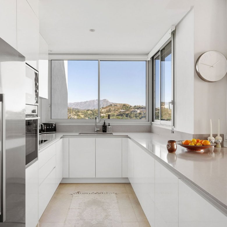 Modern white kitchen with large windows showcasing Marbella's mountain scenery.