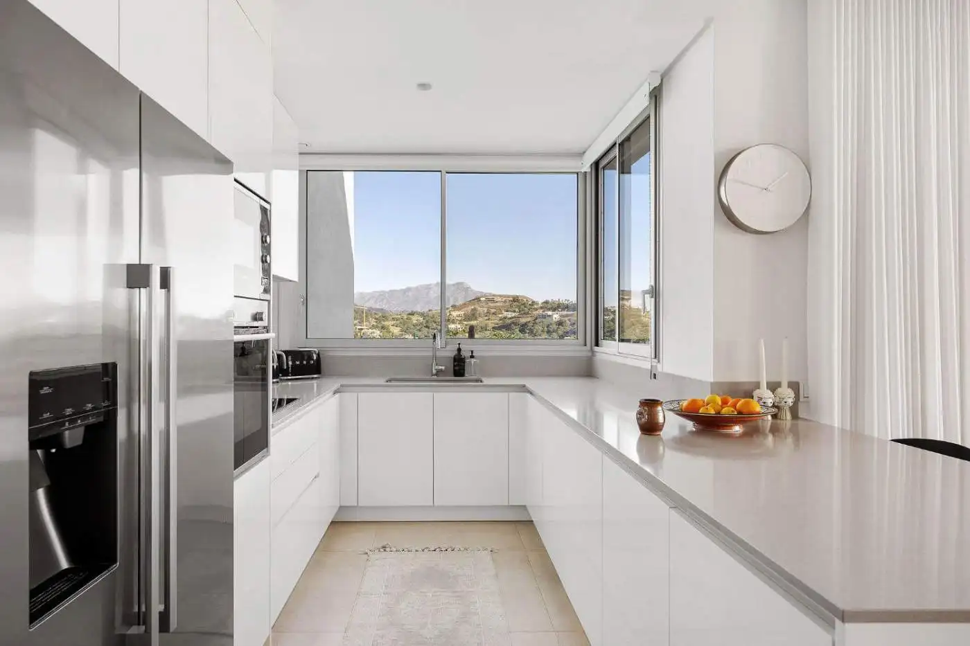 Modern white kitchen with large windows showcasing Marbella's mountain scenery.