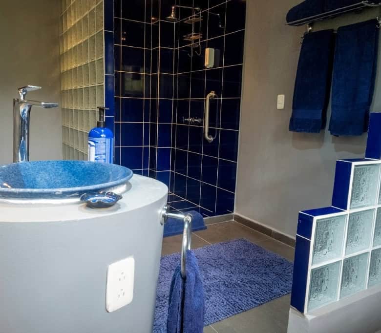 Modern bathroom featuring a blue sink, shower, and towels in a stylish setting.