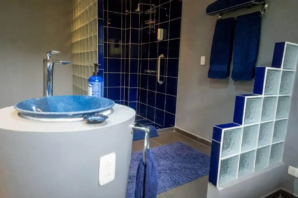 Modern bathroom featuring a blue sink, shower, and towels in a stylish setting.