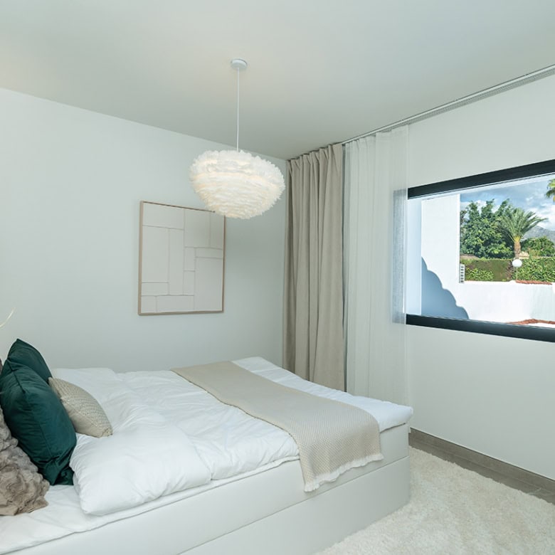 Bright bedroom in Marbella townhouse with white decor and large window view.