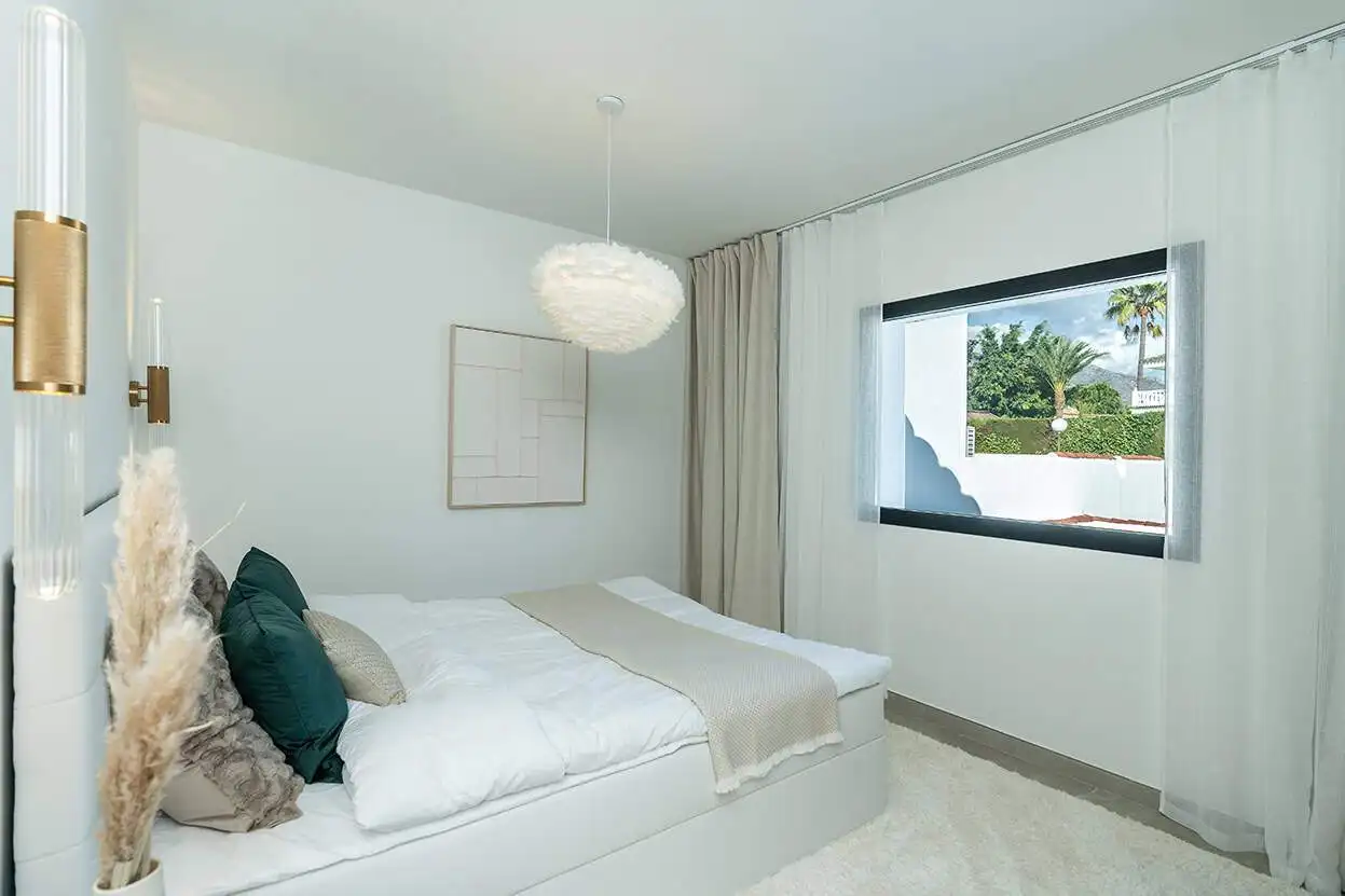 Bright bedroom in Marbella townhouse with white decor and large window view.